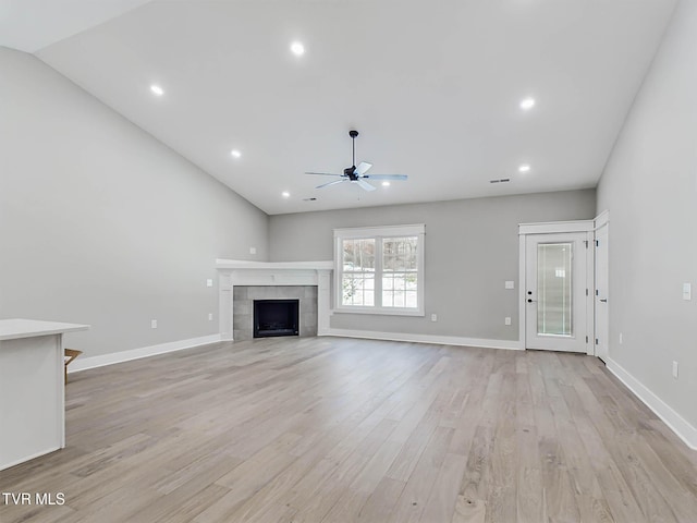 unfurnished living room with ceiling fan, light wood-type flooring, a tile fireplace, and lofted ceiling