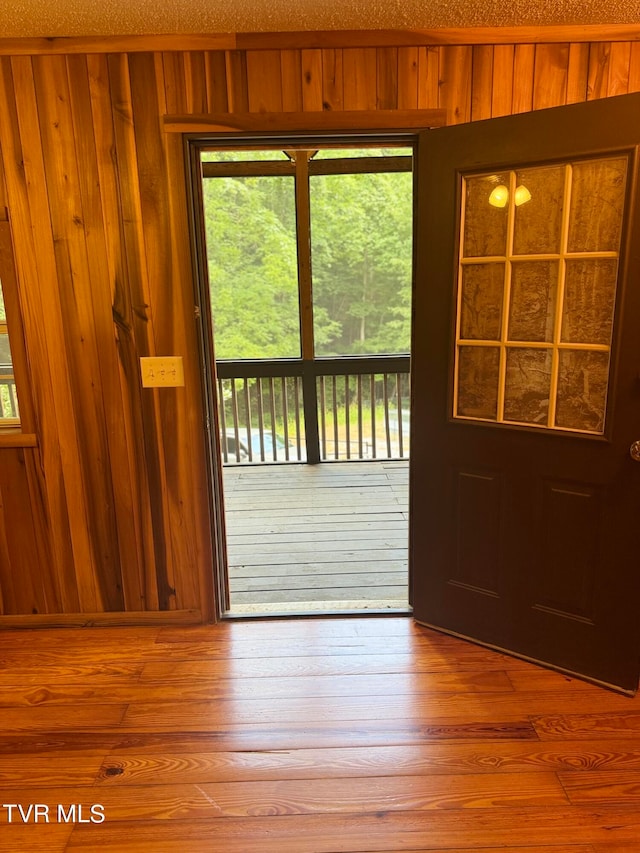 doorway featuring a textured ceiling, light hardwood / wood-style flooring, and wooden walls