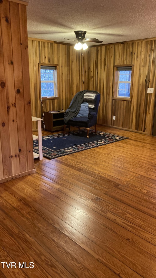 unfurnished room with wood-type flooring, a textured ceiling, ceiling fan, and wood walls