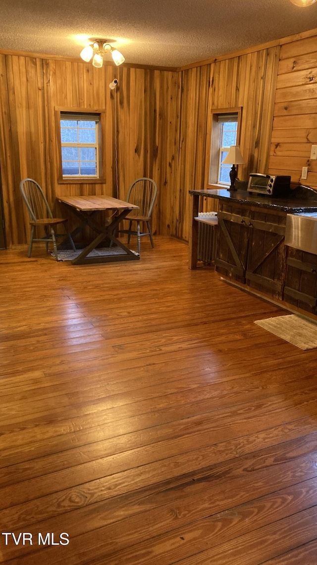 dining area featuring wooden walls, a textured ceiling, and hardwood / wood-style flooring