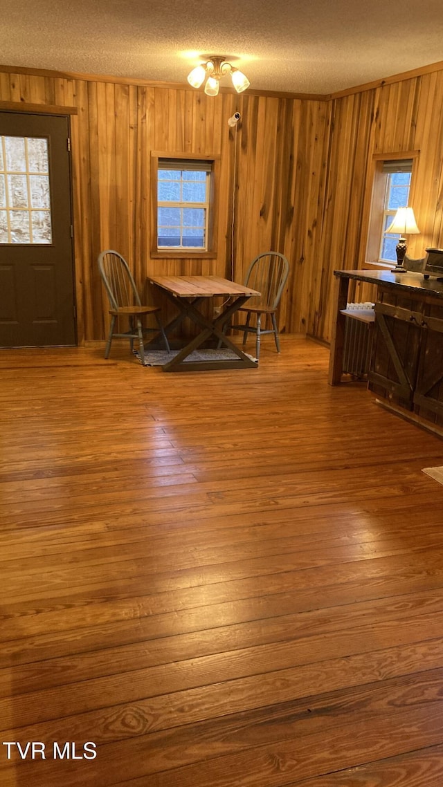 dining room featuring wooden walls, hardwood / wood-style floors, a healthy amount of sunlight, and a textured ceiling