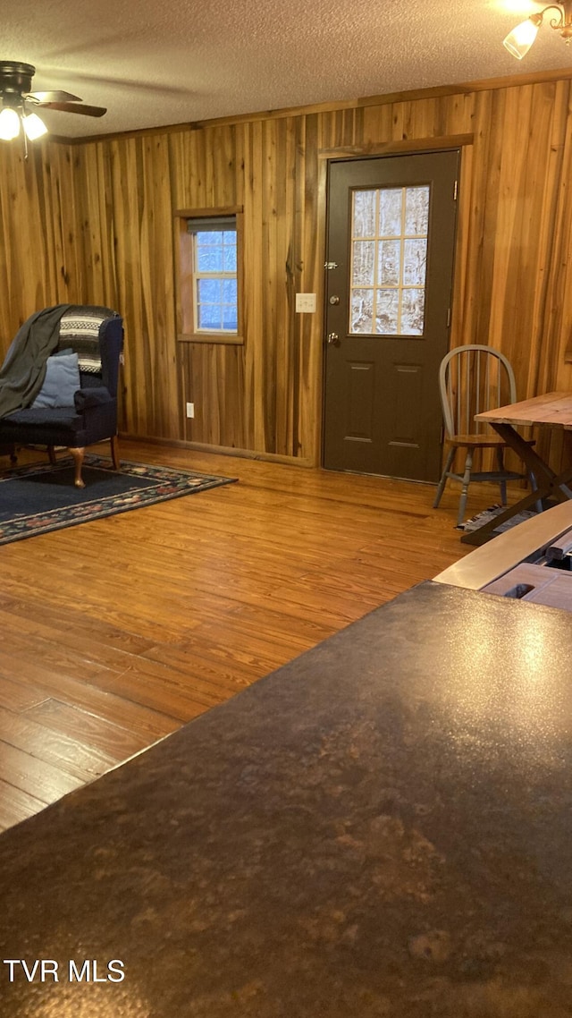 entryway featuring wood-type flooring, a textured ceiling, ceiling fan, and wooden walls