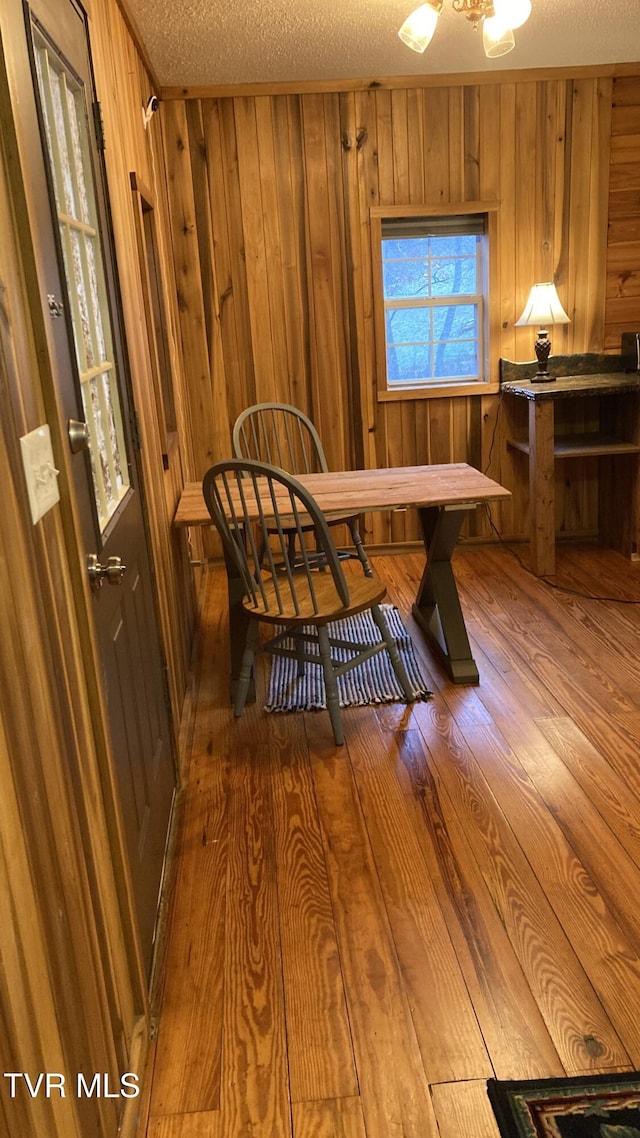 dining space with a textured ceiling, hardwood / wood-style flooring, and wood walls