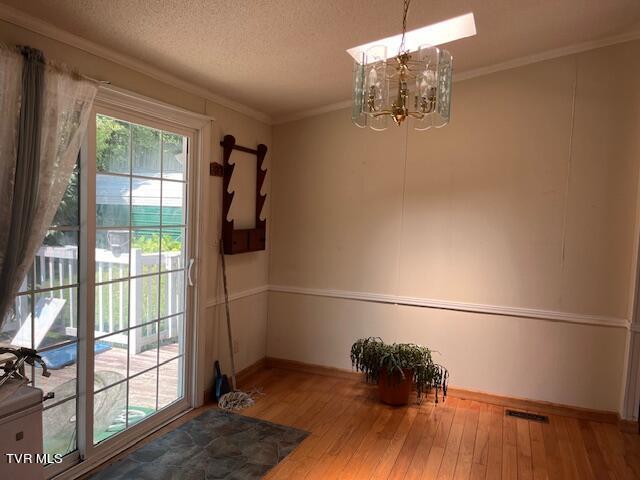 entryway featuring visible vents, ornamental molding, a textured ceiling, wood finished floors, and a chandelier