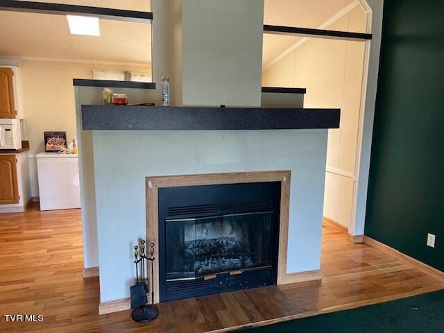 details featuring white microwave, a fireplace with flush hearth, baseboards, and wood finished floors