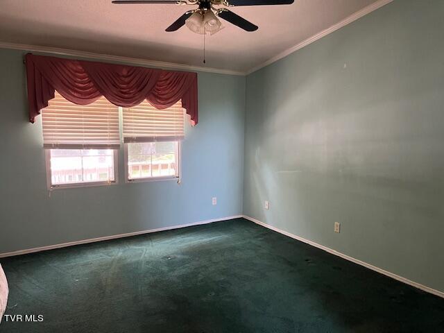 empty room with ceiling fan, dark colored carpet, ornamental molding, and baseboards