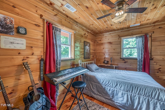 bedroom with ceiling fan, wood walls, and multiple windows