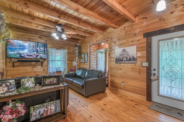 living room with light wood-type flooring, beamed ceiling, wooden walls, ceiling fan, and wooden ceiling