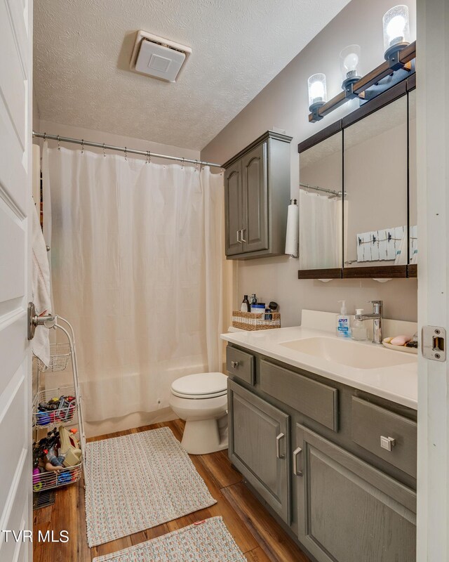 full bathroom with a textured ceiling, vanity, hardwood / wood-style floors, and toilet