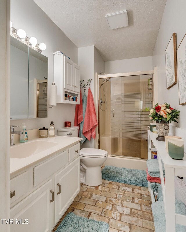 bathroom with toilet, a textured ceiling, a shower with door, and vanity