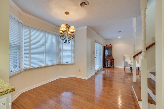 foyer with a textured ceiling, a notable chandelier, crown molding, and hardwood / wood-style flooring