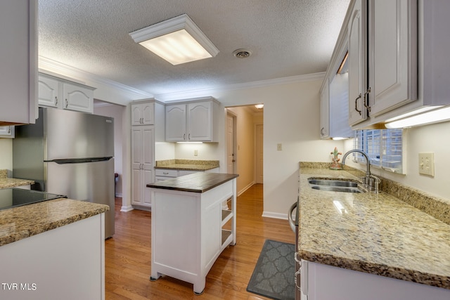 kitchen featuring dark stone counters, light hardwood / wood-style flooring, stainless steel refrigerator, white cabinetry, and sink