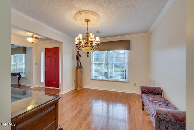 interior space featuring light wood-type flooring, a textured ceiling, a notable chandelier, and ornamental molding