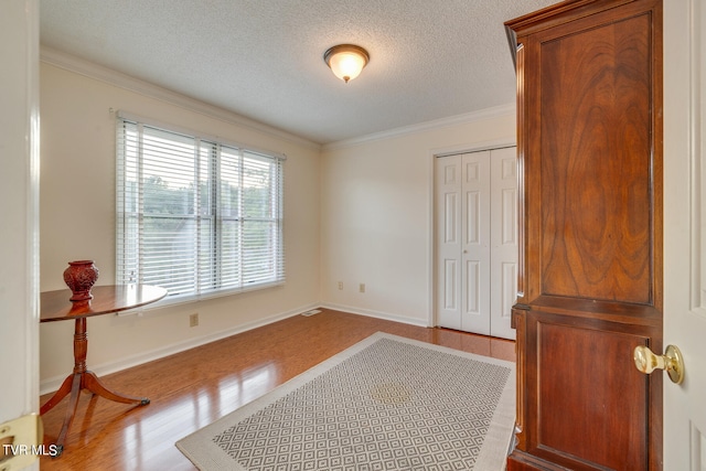 unfurnished room with a textured ceiling, light hardwood / wood-style flooring, and crown molding