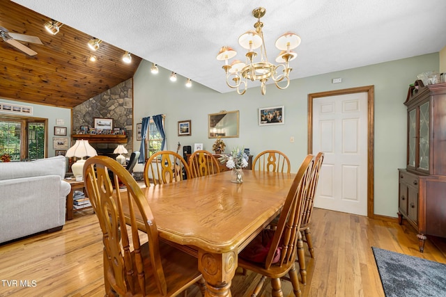 dining room featuring lofted ceiling, light wood-style flooring, a stone fireplace, a textured ceiling, and ceiling fan with notable chandelier