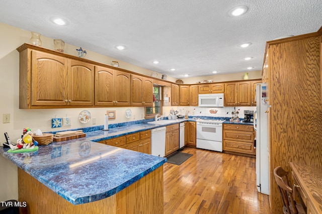 kitchen with a peninsula, white appliances, a sink, light wood finished floors, and brown cabinetry