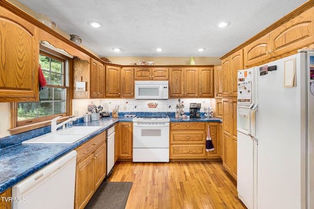 kitchen with white appliances, light wood finished floors, brown cabinetry, dark countertops, and a sink