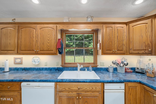 kitchen featuring brown cabinetry, dark countertops, dishwasher, and a sink