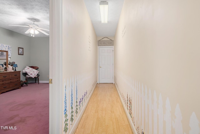 corridor featuring a textured ceiling, light wood-style floors, and baseboards