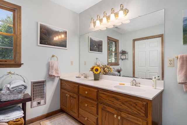 bathroom with heating unit, double vanity, baseboards, and a sink