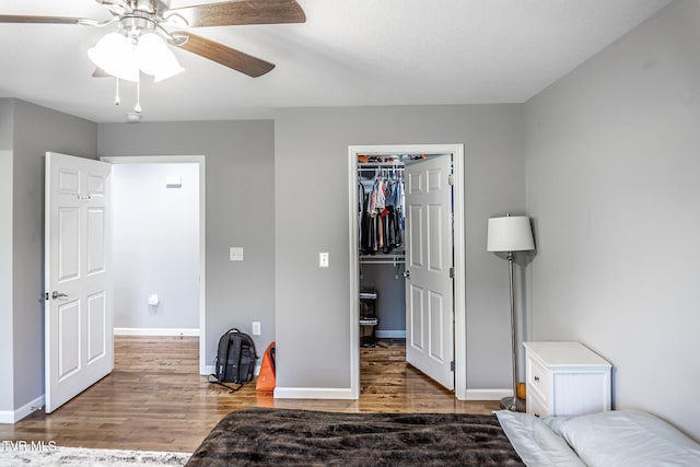 bedroom featuring baseboards, a ceiling fan, wood finished floors, a walk in closet, and a closet