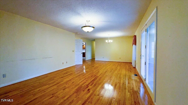 empty room with hardwood / wood-style floors, an inviting chandelier, and a textured ceiling