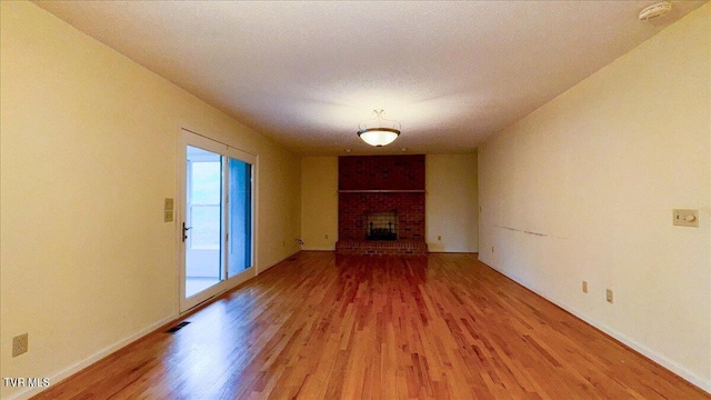 unfurnished living room with brick wall, a brick fireplace, and hardwood / wood-style floors