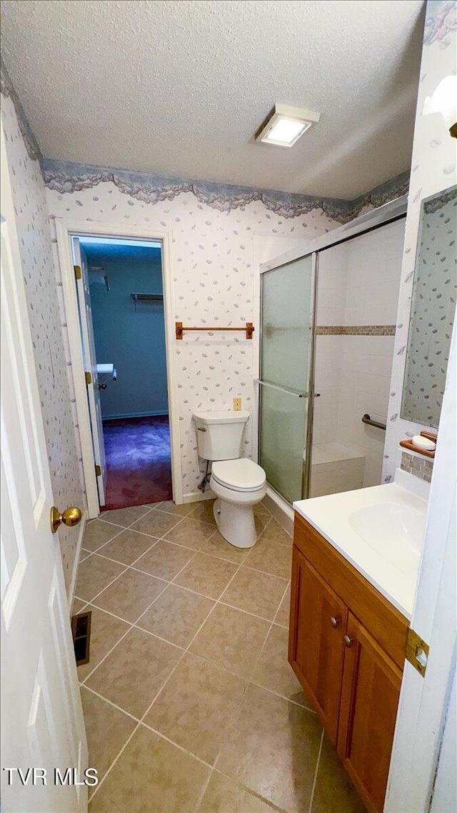 bathroom featuring tile patterned flooring, vanity, toilet, a shower with shower door, and a textured ceiling