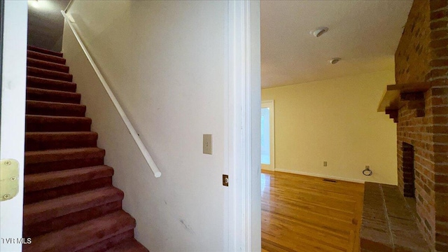 staircase featuring hardwood / wood-style flooring and a brick fireplace