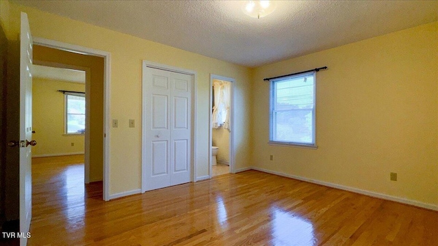 unfurnished bedroom with a textured ceiling, connected bathroom, and light hardwood / wood-style floors