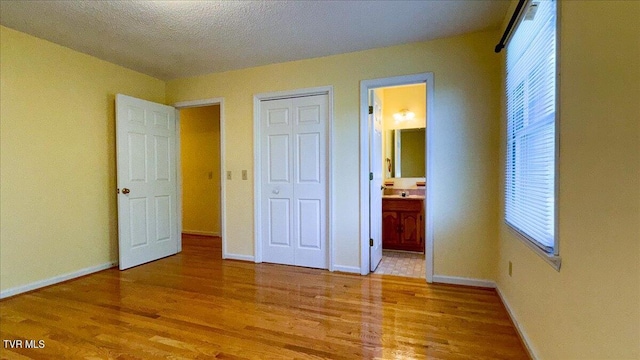 unfurnished bedroom with a textured ceiling, wood-type flooring, a closet, and ensuite bathroom