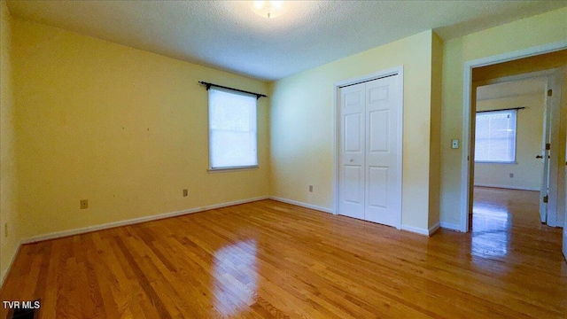 unfurnished bedroom with multiple windows, wood-type flooring, and a closet