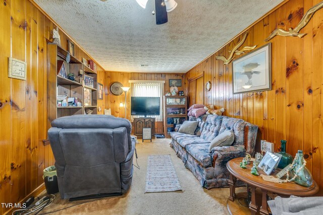 carpeted living room featuring a textured ceiling, wood walls, and ceiling fan