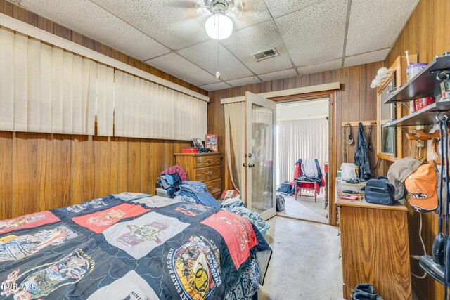 bedroom with light carpet, wood walls, a closet, and a drop ceiling