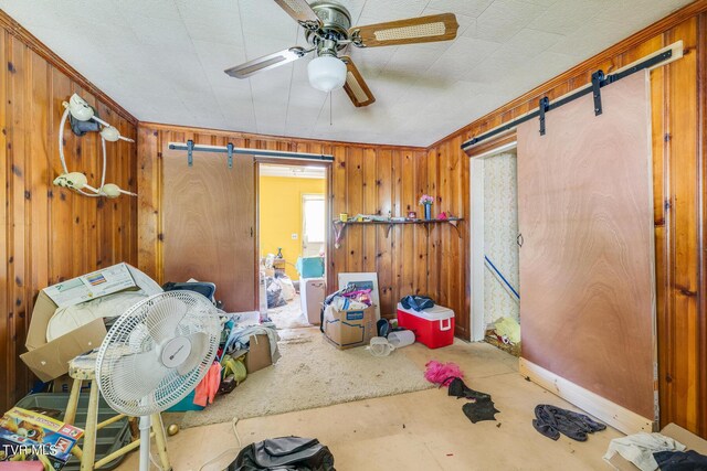 interior space featuring ornamental molding, ceiling fan, a barn door, and wooden walls