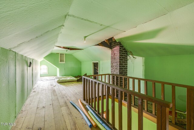 additional living space with lofted ceiling, hardwood / wood-style flooring, brick wall, and a textured ceiling