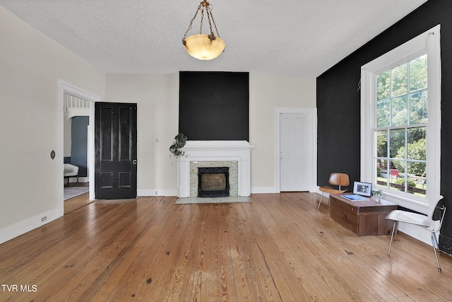 living room featuring light wood-type flooring, a textured ceiling, and a stone fireplace