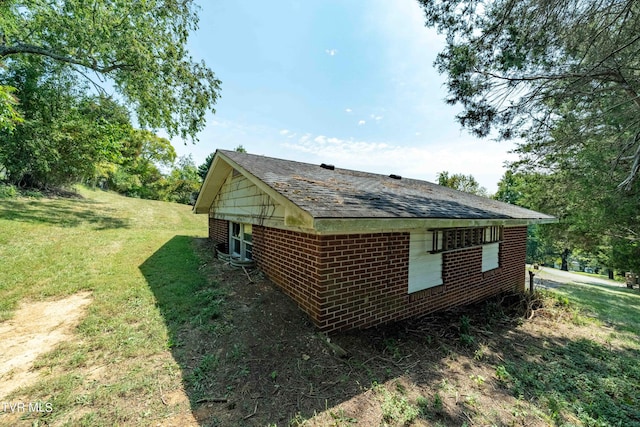 view of home's exterior featuring roof with shingles, brick siding, and a lawn