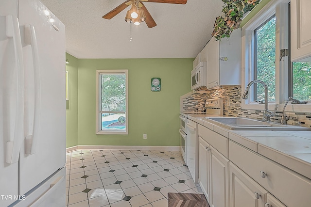 kitchen with a sink, tasteful backsplash, white cabinetry, white appliances, and ceiling fan