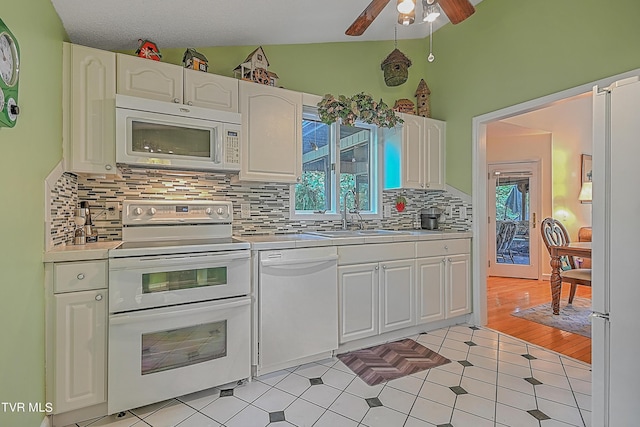 kitchen featuring white appliances, white cabinets, lofted ceiling, and a sink