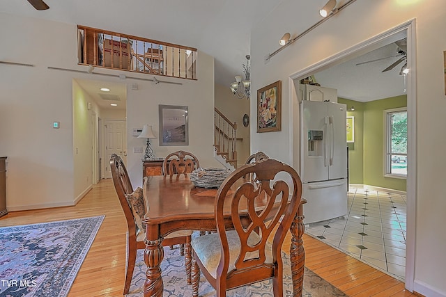 dining space with stairs, ceiling fan with notable chandelier, light wood-type flooring, and baseboards