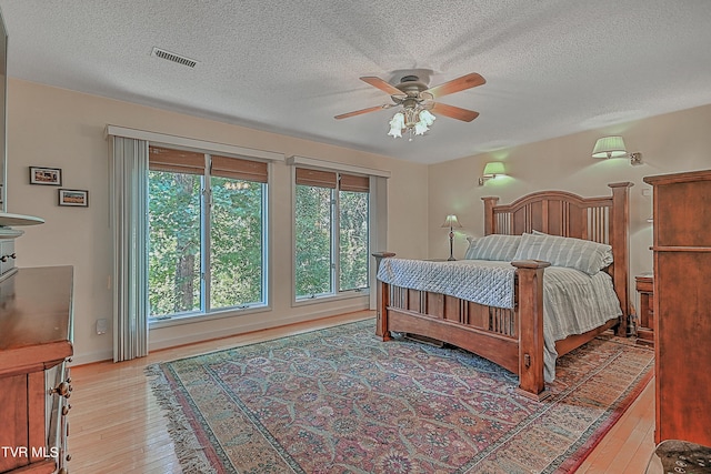 bedroom with visible vents, light wood-style flooring, a textured ceiling, and ceiling fan