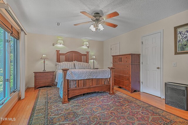 bedroom with visible vents, heating unit, a textured ceiling, light wood finished floors, and ceiling fan