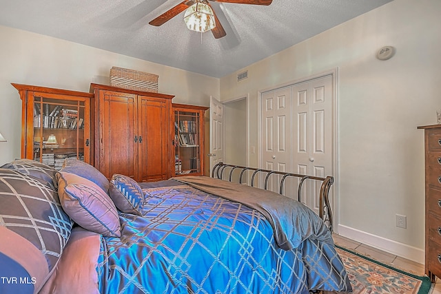 bedroom with visible vents, light tile patterned flooring, ceiling fan, a closet, and a textured ceiling