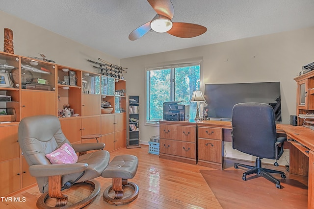 home office with a ceiling fan, light wood-type flooring, and a textured ceiling