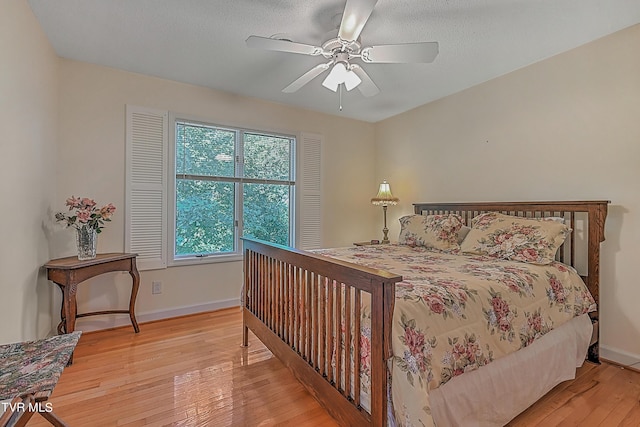 bedroom with ceiling fan, baseboards, a textured ceiling, and light wood-style flooring