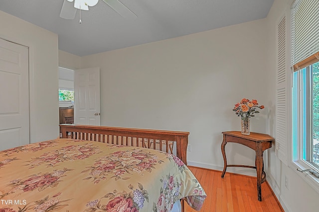 bedroom with light wood finished floors, multiple windows, a ceiling fan, and baseboards