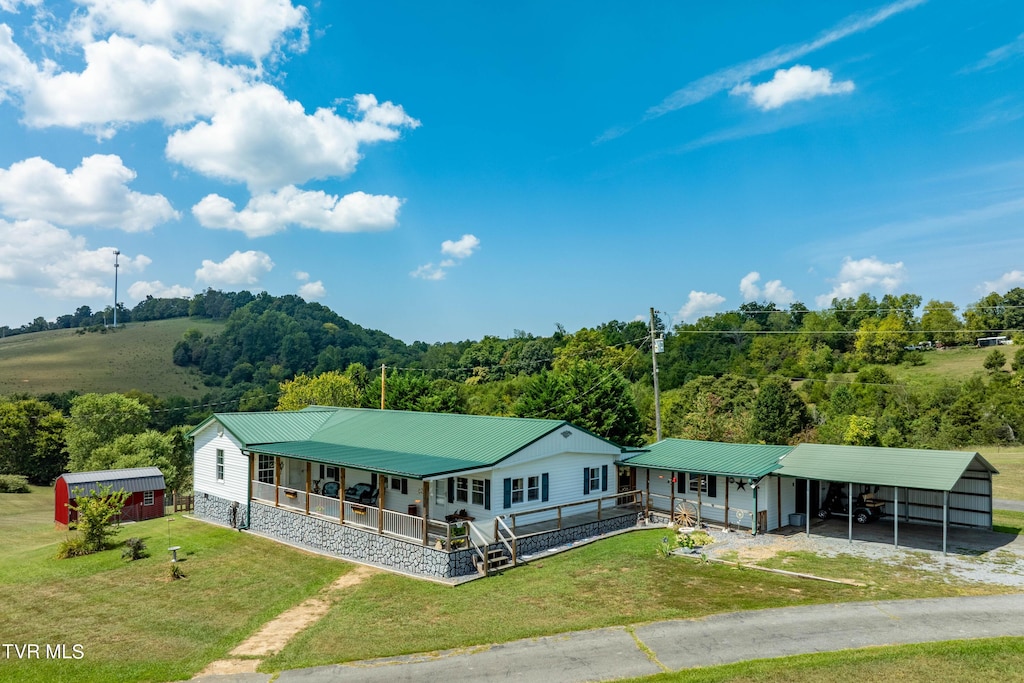 view of front of house with driveway, a carport, covered porch, a front lawn, and a wooded view