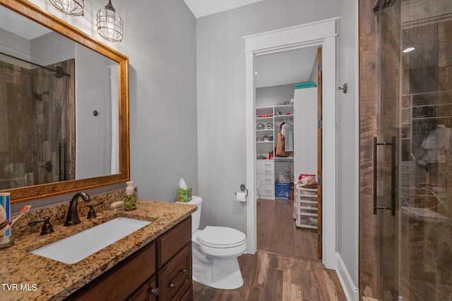 bathroom with a shower stall, a walk in closet, toilet, wood finished floors, and vanity