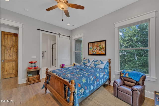 bedroom with light wood finished floors, baseboards, a barn door, and a ceiling fan